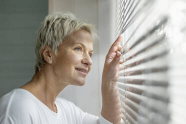 Smiling woman looking through window blinds - FSIF05882