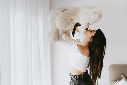 Woman kissing teddy bear in living room - MIMFF00754