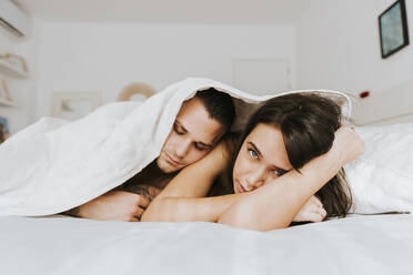 Man leaning on woman under duvet in bedroom - MIMFF00760