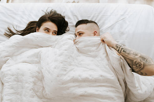 Couple under duvet looking at each other on bed - MIMFF00762