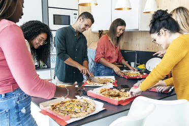 Smiling multiracial colleagues with pizzas at kitchen counter in office cafeteria - JSRF01722