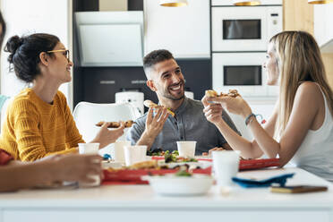 Smiling businessman with pizza talking to businesswoman at office cafeteria - JSRF01725