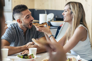 Blond businesswoman feeding pizza to businessman in office - JSRF01727