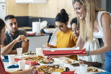 Smiling businesswoman with pizza box by colleagues in lunch break - JSRF01728