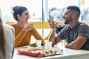 Smiling businessman eating pizza with businesswoman in lunch break - JSRF01730