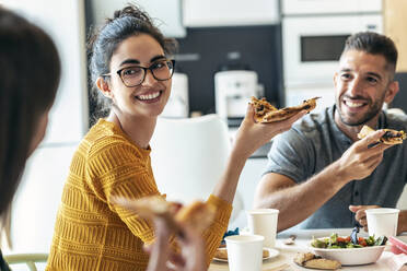 Smiling colleagues with pizza looking at businesswoman in office - JSRF01731