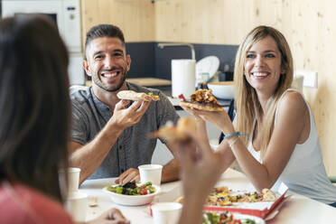 Happy colleagues looking at businesswoman with pizza in lunch break - JSRF01732