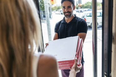 Lächelnder Pizzabote, der einer Geschäftsfrau am Eingang Pizzakartons überreicht - JSRF01733