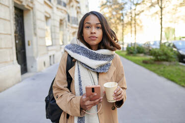 Frau mit Mobiltelefon und Kaffeetasse auf dem Gehweg - KIJF04326