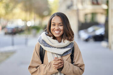 Junge lächelnde Frau trägt Tasche mit gefalteten Händen auf der Straße - KIJF04335