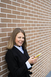 Frau hält Smartphone vor einer Backsteinmauer - GIOF14271