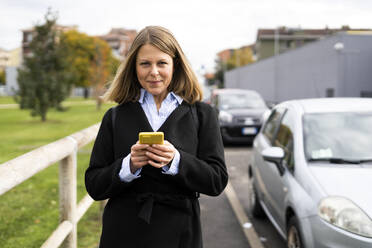 Frau in Jacke hält Handy auf der Straße - GIOF14276