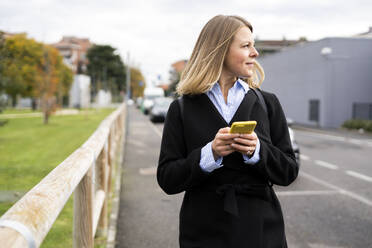 Blonde Frau hält Smartphone auf der Straße - GIOF14277