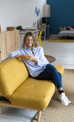 Frau mit Kaffeetasse auf Sofa im Wohnzimmer sitzend - GIOF14281