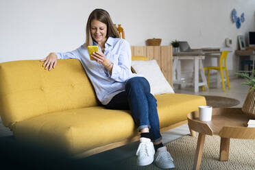 Lächelnde Frau mit Smartphone auf dem Sofa im Wohnzimmer zu Hause - GIOF14282