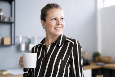 Thoughtful woman holding coffee cup at home - GIOF14298