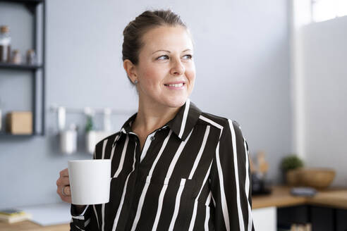 Nachdenkliche Frau hält Kaffeetasse zu Hause - GIOF14298
