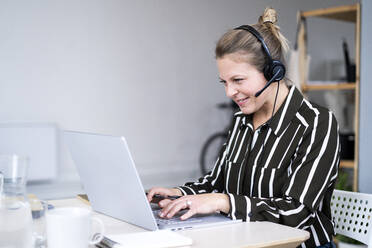 Businesswoman with headphones using laptop at home office - GIOF14307