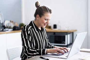 Smiling freelancer using laptop at home office - GIOF14308