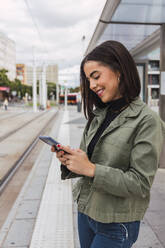 Junge Frau, die am Straßenbahnsteig ein Mobiltelefon benutzt - JRVF02084