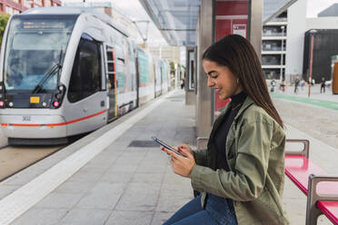 Frau benutzt Mobiltelefon an einer Straßenbahnhaltestelle - JRVF02089