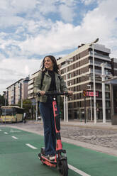 Woman riding electric push scooter in city - JRVF02098