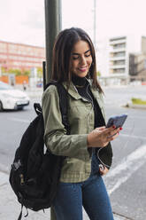 Young woman with backpack using mobile phone on road - JRVF02105