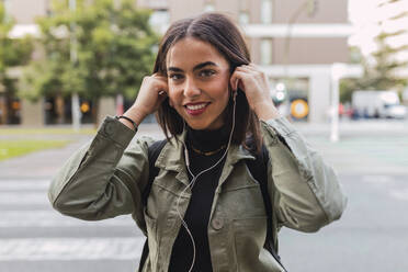 Smiling woman wearing in-ear headphones on road - JRVF02108