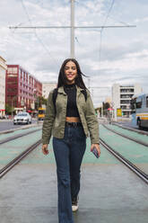 Young woman walking on tram tracks - JRVF02109