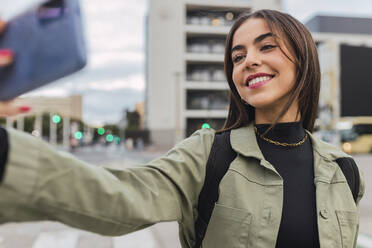 Smiling woman taking selfie through smart phone on road - JRVF02117