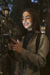 Junge Frau in Jacke, die nachts ihr Smartphone benutzt - JRVF02127