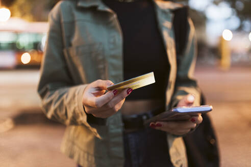 Frau mit Kreditkarte beim nächtlichen Online-Einkauf mit dem Mobiltelefon - JRVF02128