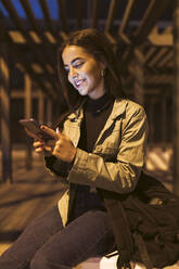 Junge Frau mit Rucksack und Mobiltelefon auf einer Bank - JRVF02131