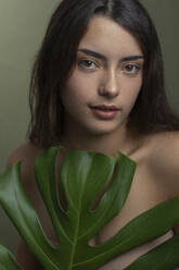 Young shirtless woman with green monstera leaf - JBYF00049