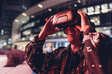 Junger Mann mit Virtual-Reality-Headset bei Nacht in der Stadt - MEUF04906