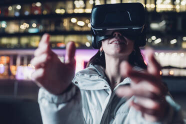 Frau mit Virtual-Reality-Headset gestikuliert bei Nacht - MEUF04908