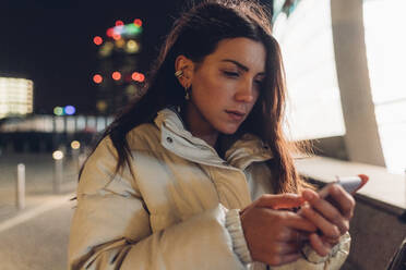 Junge Frau, die nachts an der Wand ein Mobiltelefon benutzt - MEUF04909