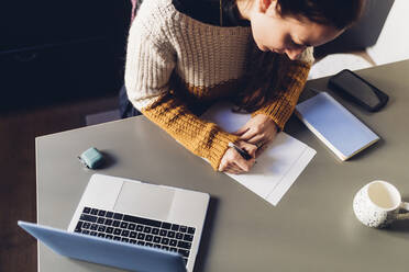 Businesswoman writing on page at home office - MEUF04914