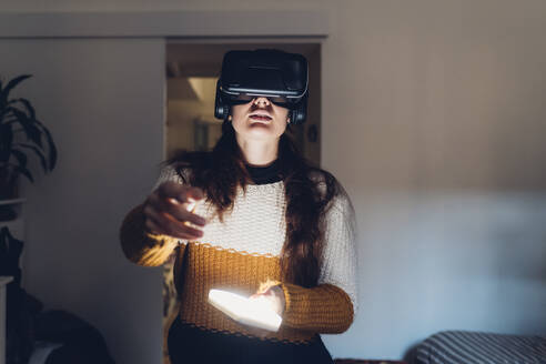 Frau mit LED-Licht trägt Virtual-Reality-Headset zu Hause - MEUF04920
