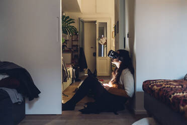 Woman with virtual reality headset sitting by wall at home - MEUF04922