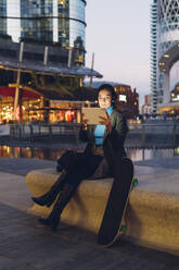 Geschäftsfrau hält Tablet-PC durch Skateboard sitzen auf Bank in der Stadt - MEUF04943