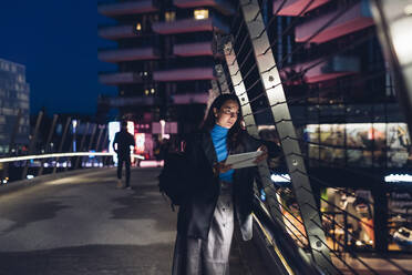 Geschäftsfrau mit Tablet-PC, die auf einer Brücke in der Stadt lehnt - MEUF04952