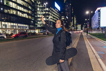 Businesswoman with skateboard hailing ride in city - MEUF04973