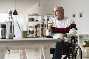 Älterer Geschäftsmann mit Trinkglas und Blick auf den Laptop auf dem Tisch - GIOF14347