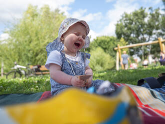Süßes Baby Mädchen mit geschlossenen Augen lachend auf Picknickdecke im Park - LAF02724