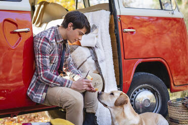 Junger Mann füttert Apfel an Hund im Wohnmobil - EIF02428