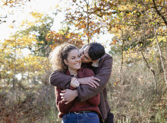 Young man kissing girlfriend in autumn forest - EIF02439