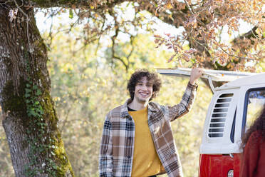 Smiling young man standing at campervan - EIF02453