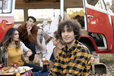 Lächelnder Mann mit Freunden, die sich beim Picknick vor einem Lieferwagen unterhalten - EIF02471