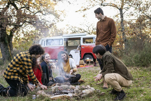 Glückliche Freunde beim Picknick im herbstlichen Wald, die Würstchen braten - EIF02484